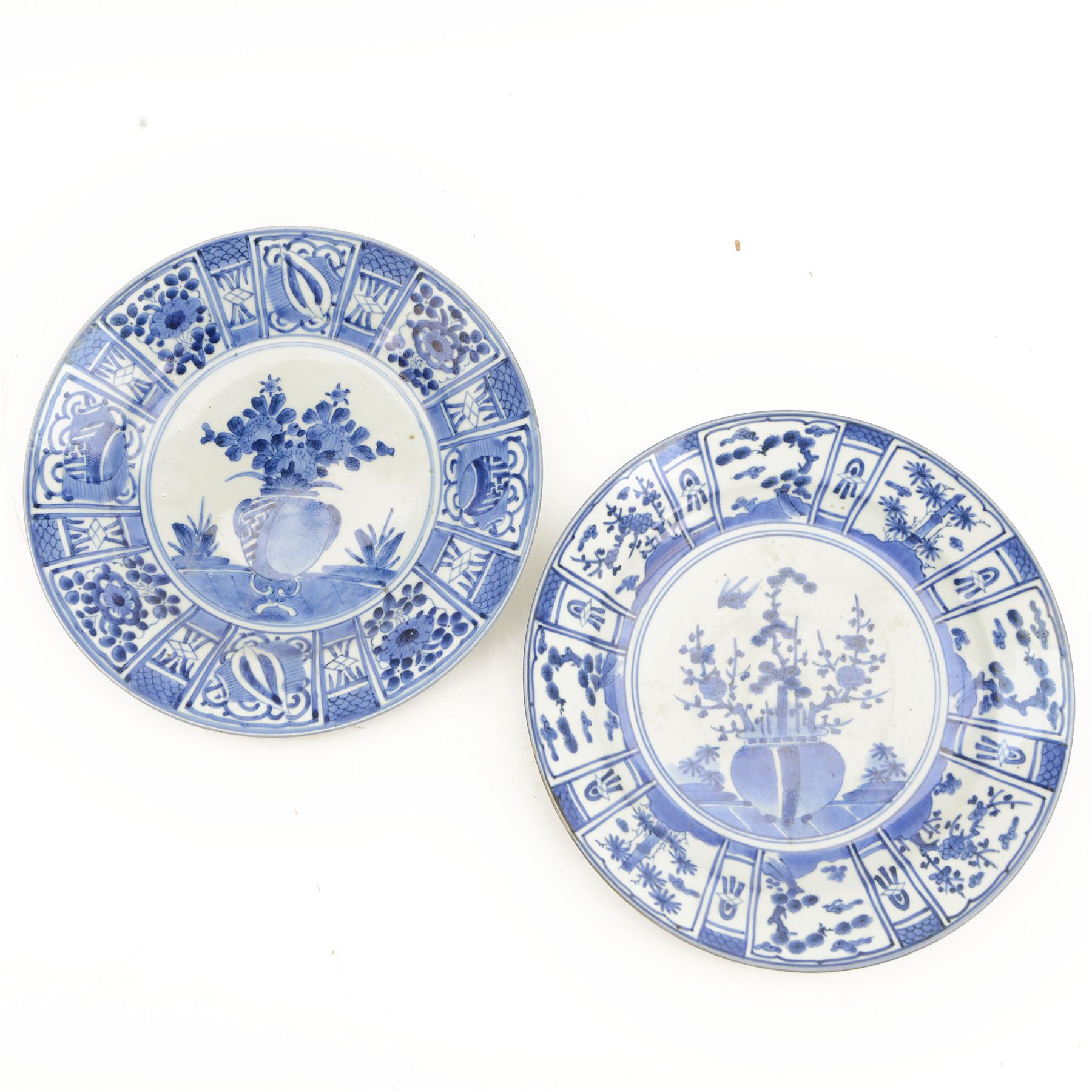 Two Japanese Edo period Ko Imari blue and white porcelain chargers, each decorated in the Kraak style with urns issuing peonies, pine and prunus, within panelled borders containing flowers, tress and precious objects, each approximately D 31.5cm