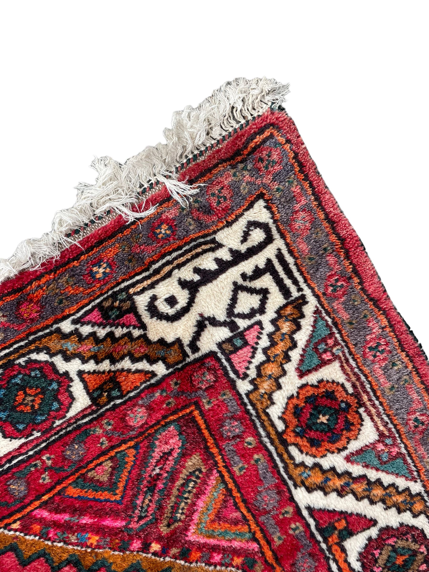 Persian Hamadan red ground rug, decorated with six stepped lozenge medallions, the guarded border with repeating stylised flower head decoration, with inscription to corner