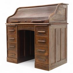 Early 20th-century oak roll-top desk with tambour shutter, enclosing a fitted interior of pigeon holes and small drawers, and pedestal base fitted with nine drawers with moulded handles, raised on plinth base 
