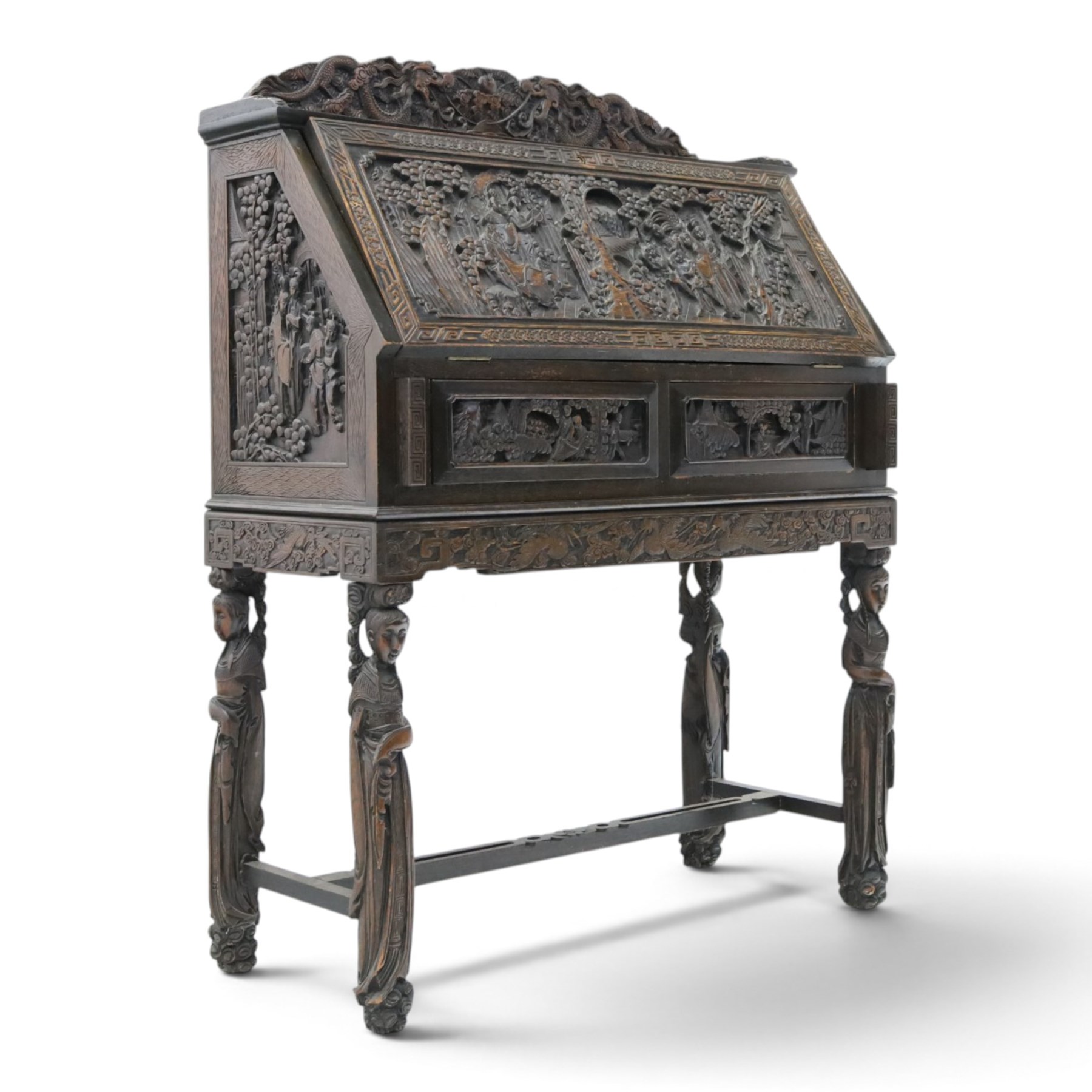 Early 20th century Chinese export carved hardwood writing bureau, the sloped fall front deeply carved with a narrative figural scene beneath pine and prunus trees, above a pair of rectangular carved panels, the shaped crest rail with entwined dragons, interior fitted with pigeonholes and a central drawer, on figural front supports with shaped stretcher