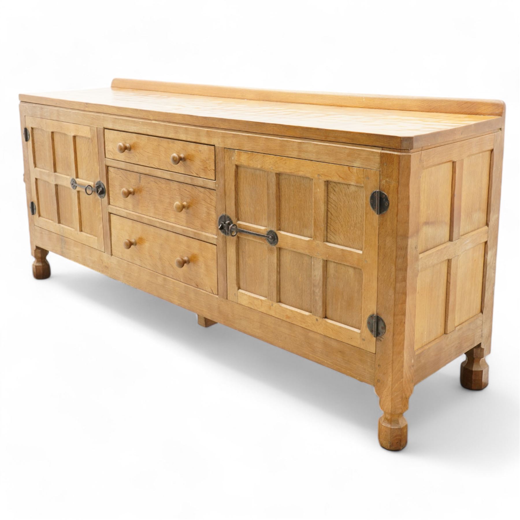 Mouseman - adzed and panelled oak 6' sideboard, fitted with four central drawers and flanking cupboards, enclosed by two panelled doors with wrought metal latches and hinges, on octagonal feet, carved with mouse signature, panelled sides, by the workshop of Robert Thompson, Kilburn 