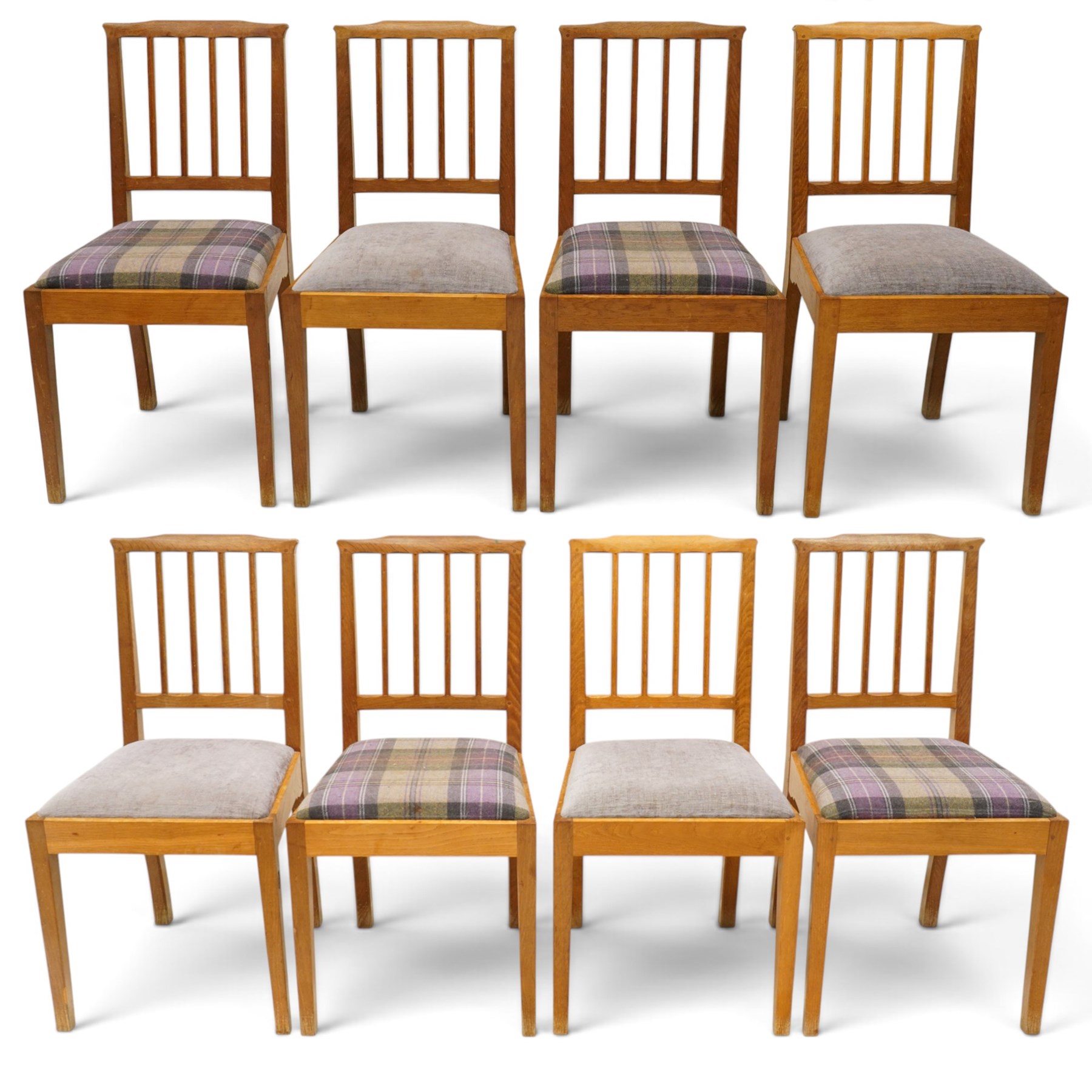 Acorn Industries - set of eight oak dining chairs, the shaped cresting rail over a fluted stick back, the drop-in seats upholstered in contrasting form with four pale mauve and four in purple tartan, raised on square supports, carved with acorn signature, by Alan Grainger, Brandsby