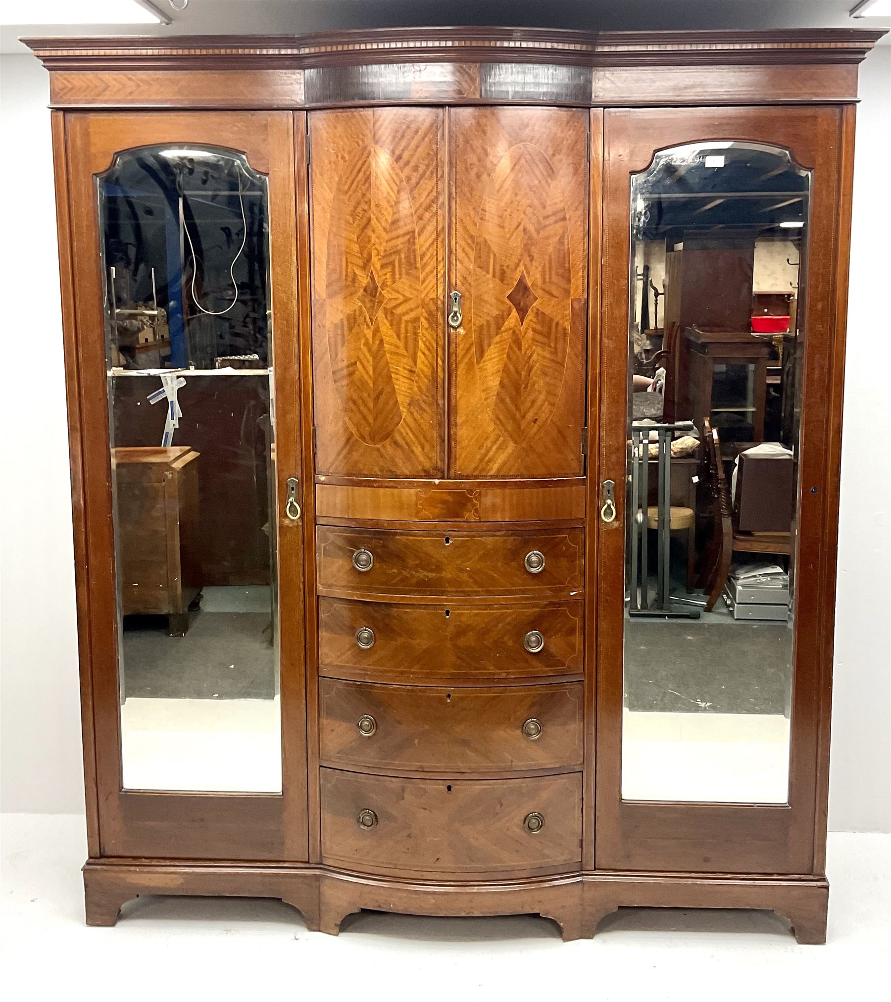 Edwardian inlaid mahogany triple wardrobe, bow front centre with two cupboards above four graduating drawers flanked by two bevel edged mirror doors, shaped platform base 