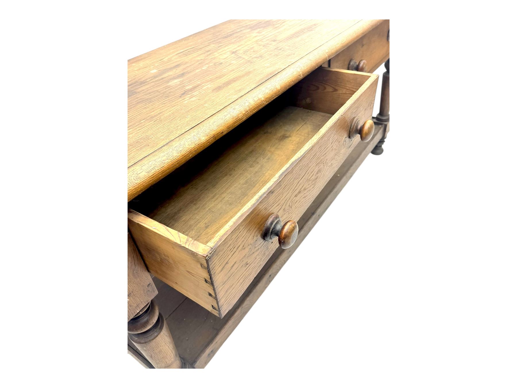 Late 19th century oak potboard dresser base, rectangular top over two frieze drawers with turned wooden handles, raised on four ring turned and tapering supports with block feet, united by a full-width lower potboard