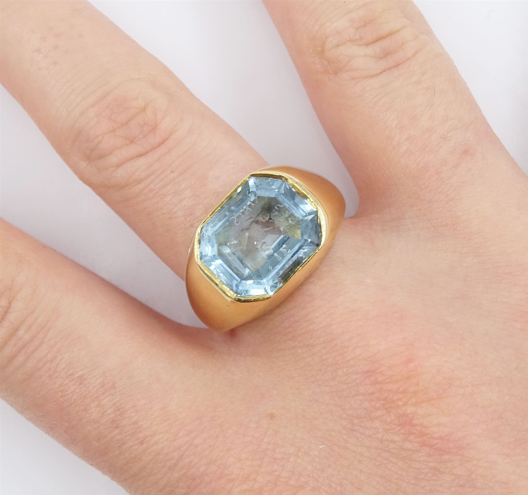 Early 20th century 18ct gold bezel set octagonal cut aquamarine intaglio ring, with Cupid as a blacksmith forging two hearts, Birmingham 1919
