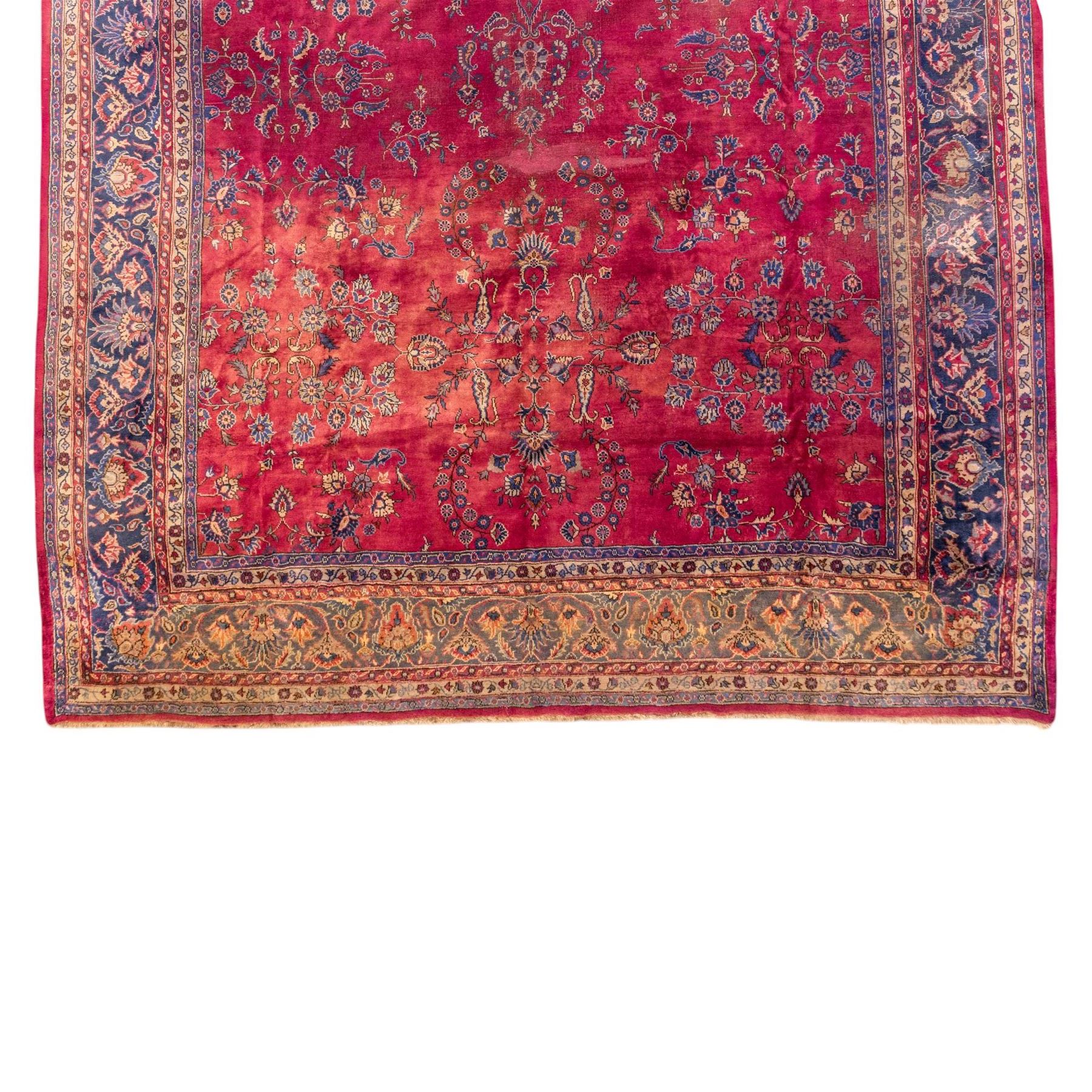 Large Persian-style mahal-type hand-knotted carpet, of rectangular form with a deep crimson field decorated with an all-over arrangement of stylized floral sprays and palmettes, with a central subtle medallion composition enclosed by a dark navy main border of scrolling floral motifs between narrow guard stripes with fringe ends 