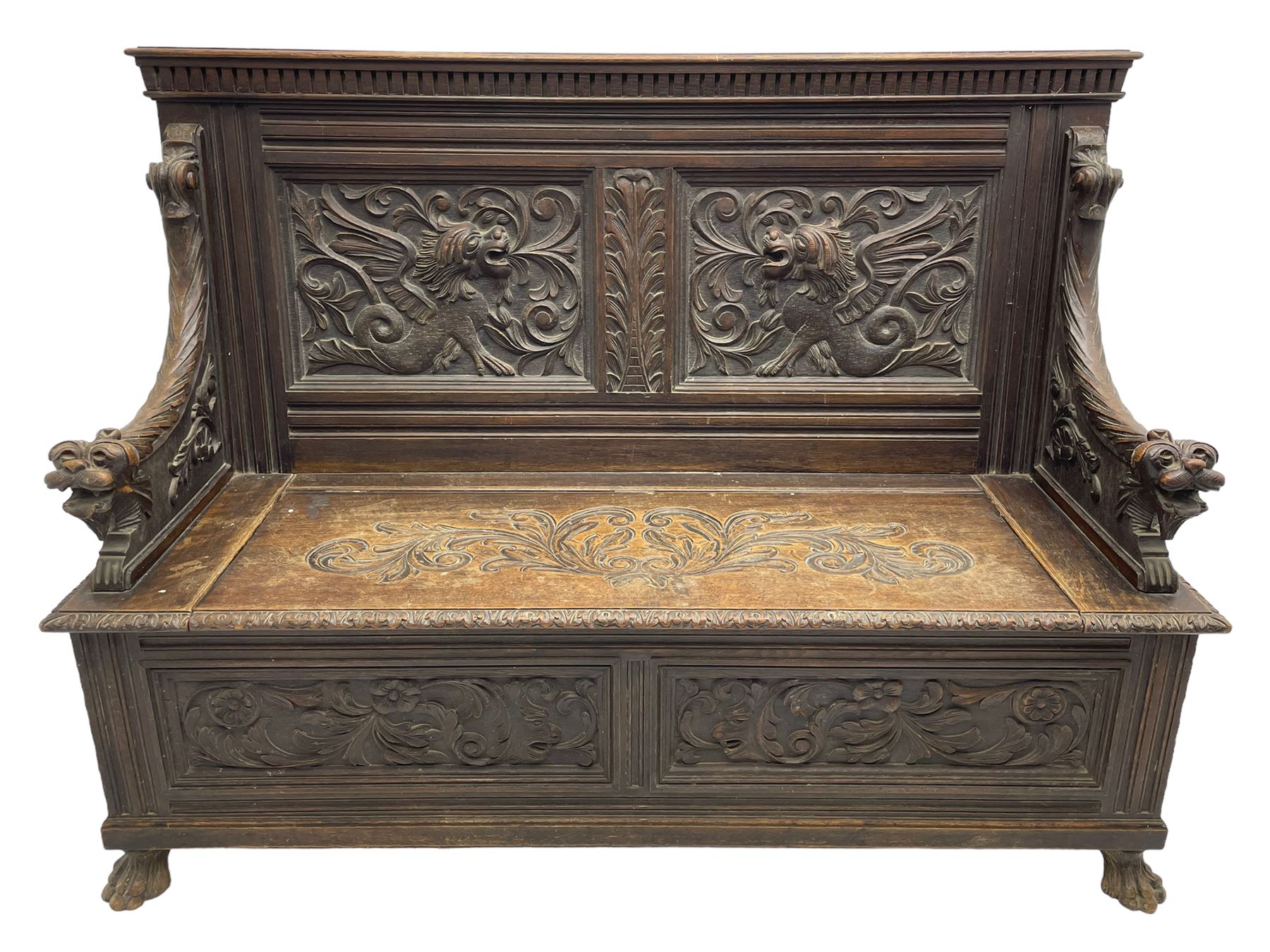 19th century oak hall bench, dentil cresting rail over moulded frame with panelled back carved with fire-breathing mythical beasts and central acanthus leaf motif, scroll carved down-sweeping arms carved with grotesque masks with scrolled foliage and shells, hinged box seat carved with scrolling foliage over panelled front with further carved foliage decoration, on paw carved front feet 