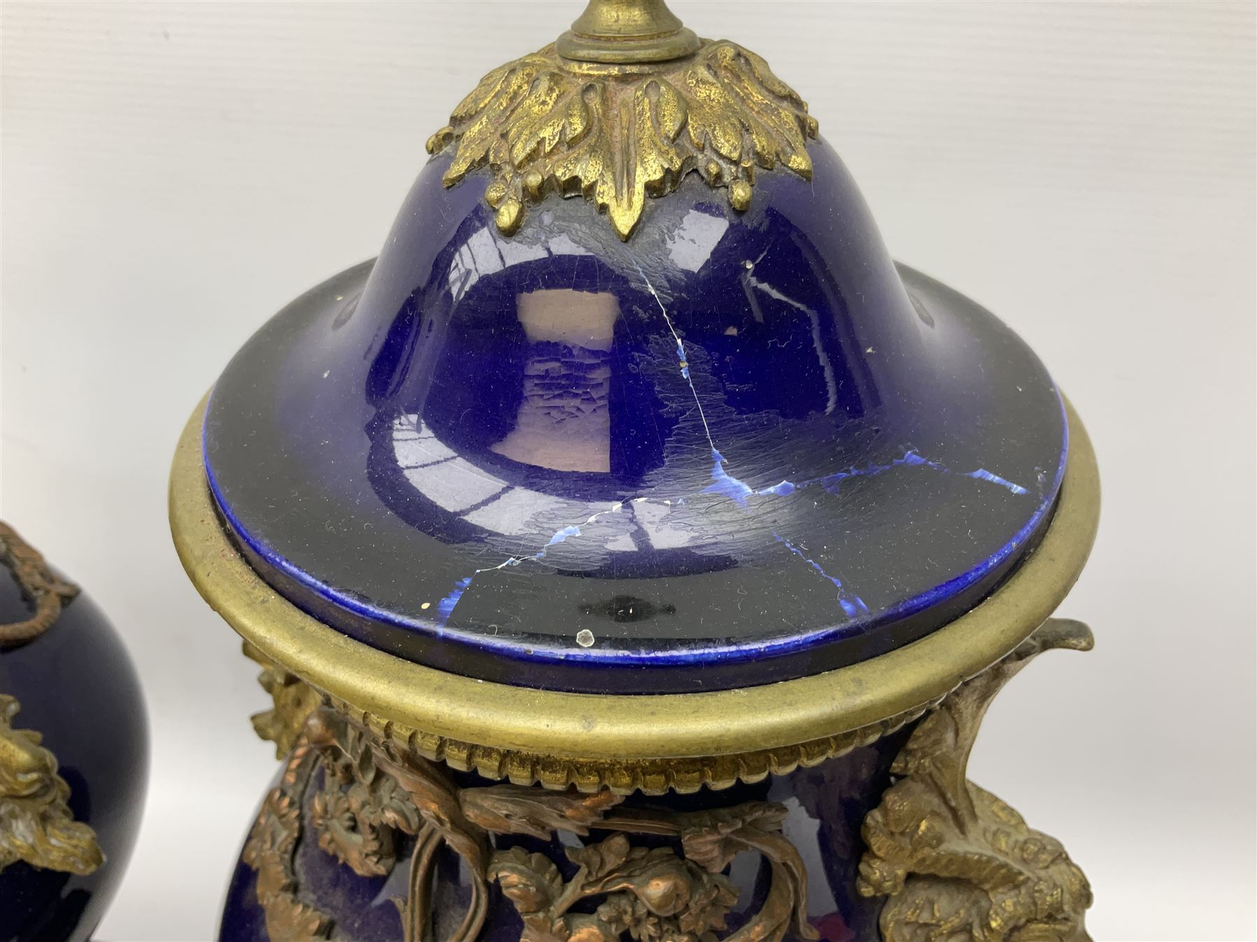 Pair of French large cobalt blue lidded urns, probably 19th century, the body decorated with ormolu ram's heads and ornate foliate design, the domed cover with brass berry finial, raised upon pedestal base with beaded decoration upon shaped plinth, H52cm