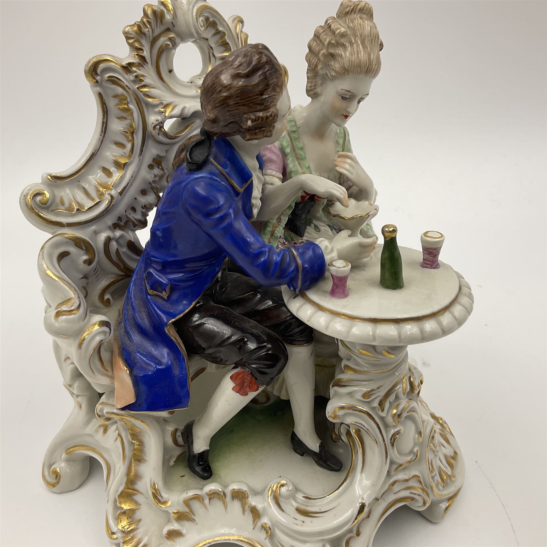 Figure group, probably Volkstedt, modelled as a courting couple seated before a table, the ornate bench and table conforming with and leading from the gilt heightened scrolling base, with blue painted mark beneath, H14.5cm
