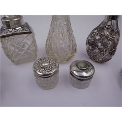 Two silver mounted dressing table jars, one in the form of a heart, both with embossed silver covers and cut glass bodies, hallmarked, together with two smaller examples, one set with mother of pearl, three silver mounted glass scent bottles, including an example with prunus blossom decoration, stamped Sterling, tallest bottle H17cm
