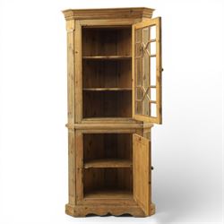 19th century stripped pine corner cabinet, projecting cornice flanked by fluted sides, astragal glazed upper door with brass knob, lower section with fielded panelled door, raised on a shaped plinth base 