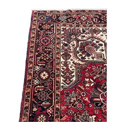 Persian Heriz red ground rug, central scrolled medallion on dark ground decorated with floral motifs, the surrounding field decorated with stylised plant motifs and smaller geometric symbols, guarded border with repeating pattern punctuated with rosettes and flower heads 