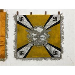 Two replica German Luftwaffe trumpet banners, one heavily silver wire embroidered with Luftwaffe eagle in a wreath, on an amber, white and black rayed background, , with silver wire tasselled border and four leather hanging loops, approx. 50 x 49cm; the other slightly larger heavily gold wire embroidered with the Luftwaffe eagle on a plain amber ground with gold wire tasselled border and two hanging loops (2)