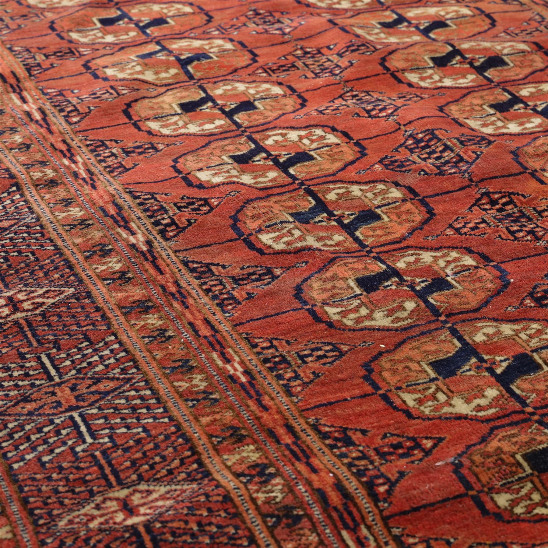 Central Asian Turkmen Tekke hand-knotted rug, madder red field decorated with rows of octagonal guls linked by secondary motifs within a dense geometric border, with fringe ends  