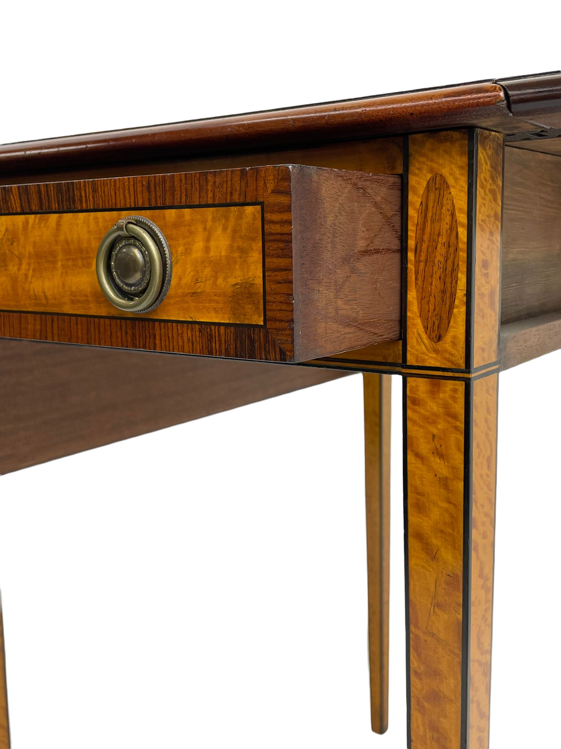 Mid-to-late 20th century Sheraton style satinwood Pembroke table, the drop leaf top with segmented veneers and central oval panel with ebony stringing, crossbanded in rosewood and with edge moulding, single short drawer to one end and faux drawer to other, square tapering supports
