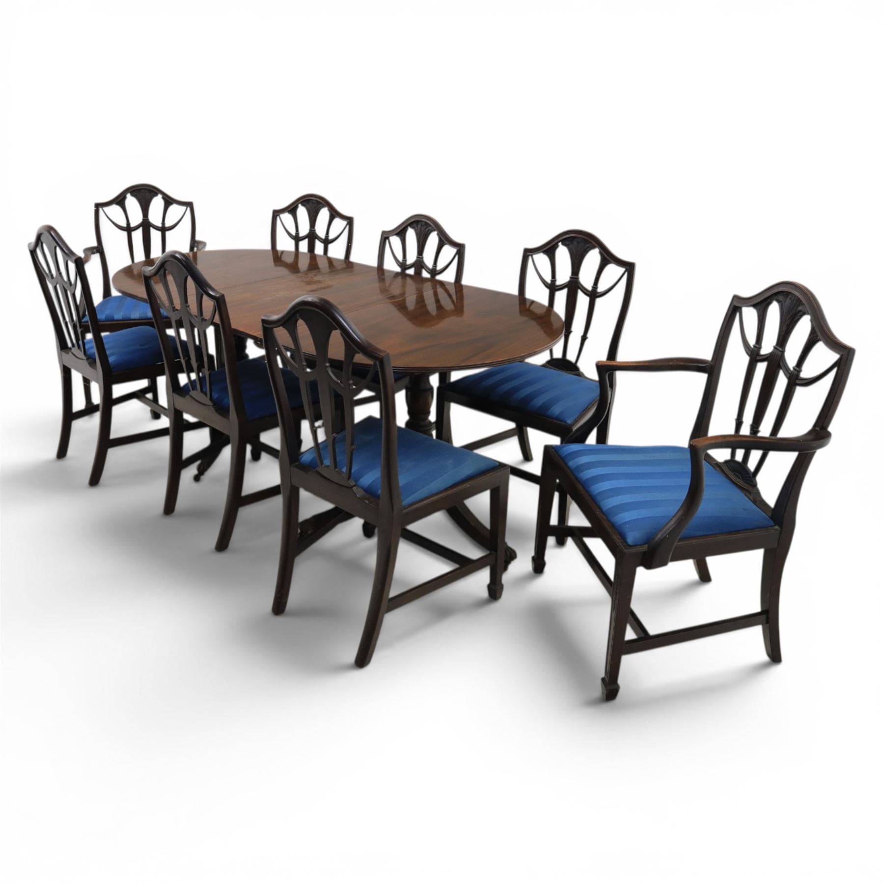 Set of eight George III style mahogany dining chairs, comprising two carvers and six singles, each with shaped top rail above pierced splay carved with feathers, with drop in stuffover seats upholstered in blue striped fabric, raised upon square tapering legs joined by stretchers, together with a mahogany twin pedestal dining table, the oval top with central leaf raised upon turned columns and splayed reeded legs terminating in lion paw feet and brass castors, 