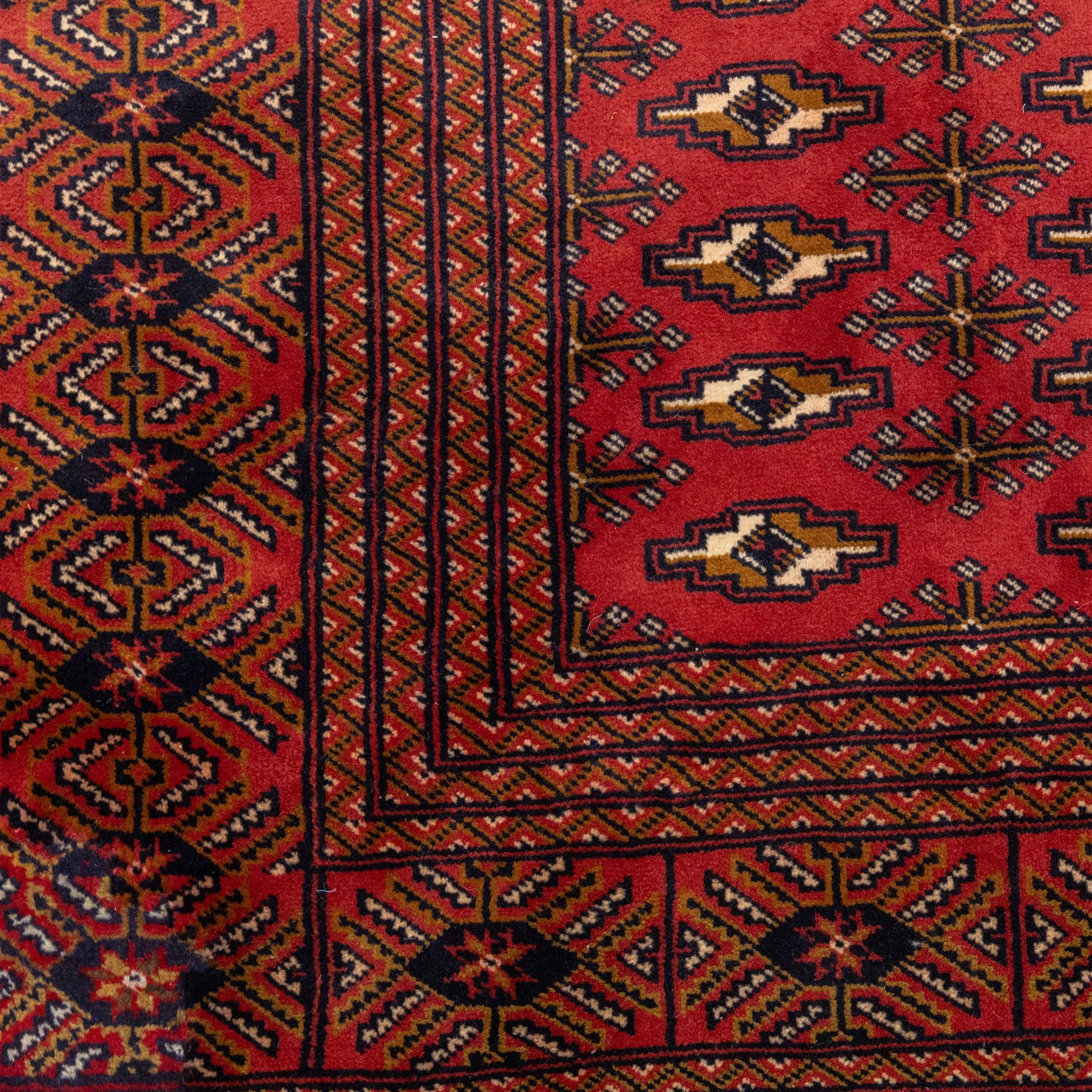 North East Persian Turkoman hand-knotted carpet, madder red field decorated with rows of repeating Tekke guls, in offset horizontal bands and interspersed cruciform subsidiary motifs, enclosed within narrow geometric borders featuring stylized tribal devices, with fringe ends   