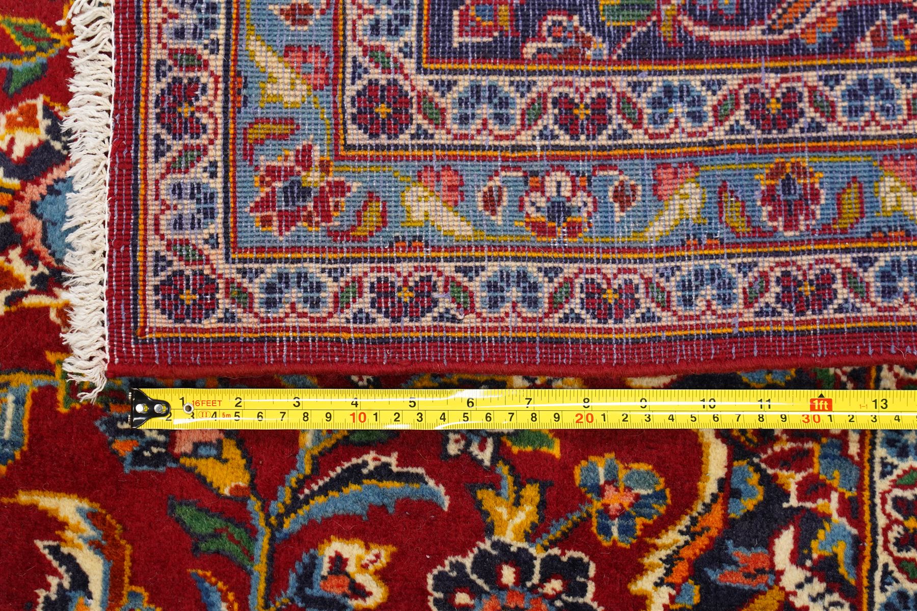 Central Persian Kashan hand-knotted carpet, crimson field with central cusped medallion in ivory, pale blue and indigo, issuing a network of scrolling arabesques, palmettes, and floral sprays, with conforming spandrels, main border of scrolling vinery and stylized palmettes, framed by multiple guard borders, with cotton fringe ends 