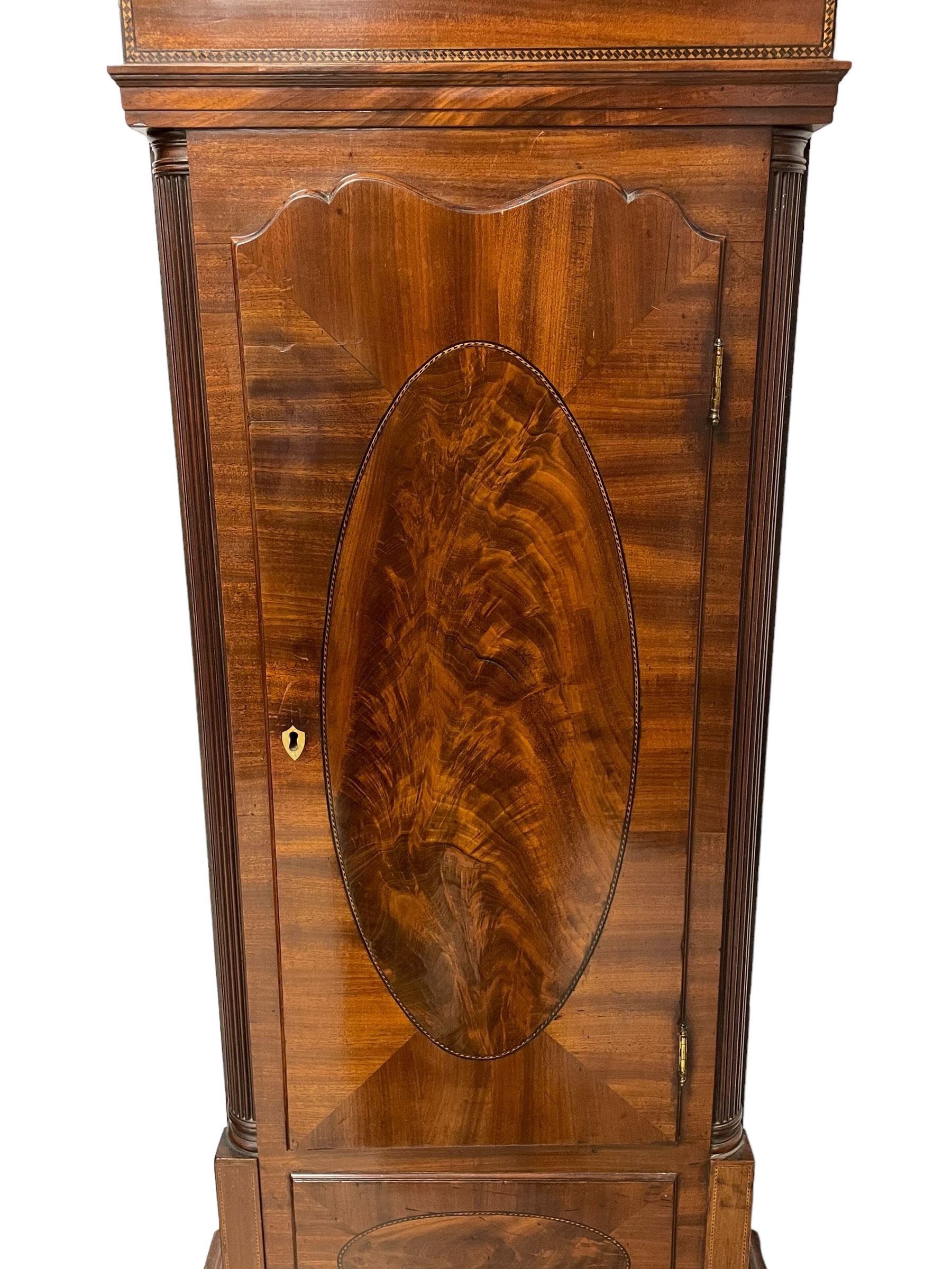 John Morgan of Aberystwyth - fine George IV mahogany 8-day longcase clock c1820, with a raised swan necked pediment, ball and eagle finial and deep inlaid frieze beneath, square hood door with a glazed circular wooden bezel and canted corners, long trunk with reeded quarter columns and a wavy topped door, rectangular plinth on bracket feet, circular painted dial with Roman numerals, minute track, makers name, and brass stamped hands, rack striking four pillar movement with a recoil anchor escapement, striking the hours on a bell. With weights and pendulum. 
John Morgan is recorded as working in Aberystwyth 1816-35. 