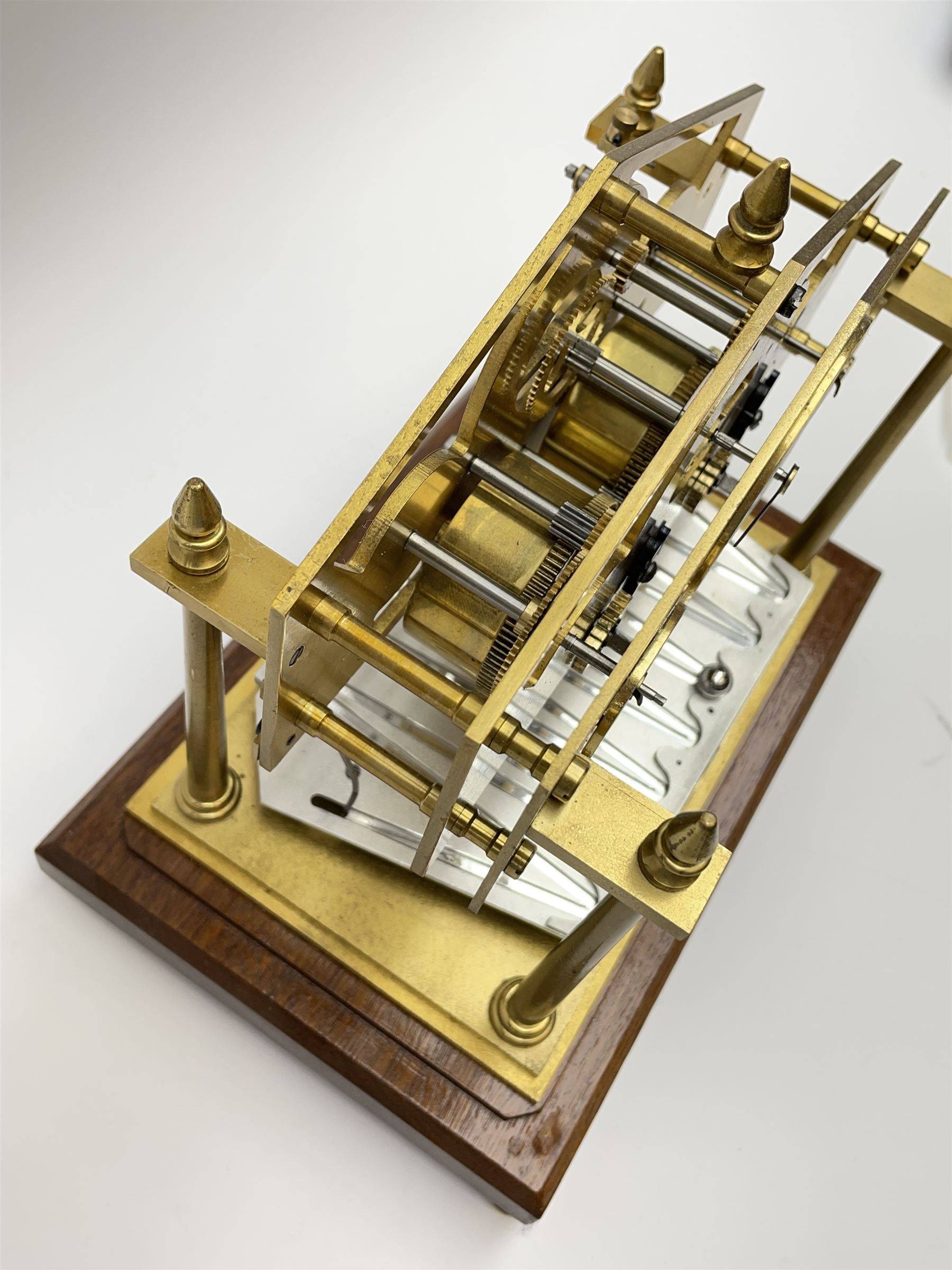Mid 20th century 'Congreve' rolling ball clock, sloped arch and pierced brass movement, the central Arabic minute chapter ring flanked by hour and seconds dials, twin train driven eight day movement, raised on mahogany plinth with turned brass feet, under acrylic cover