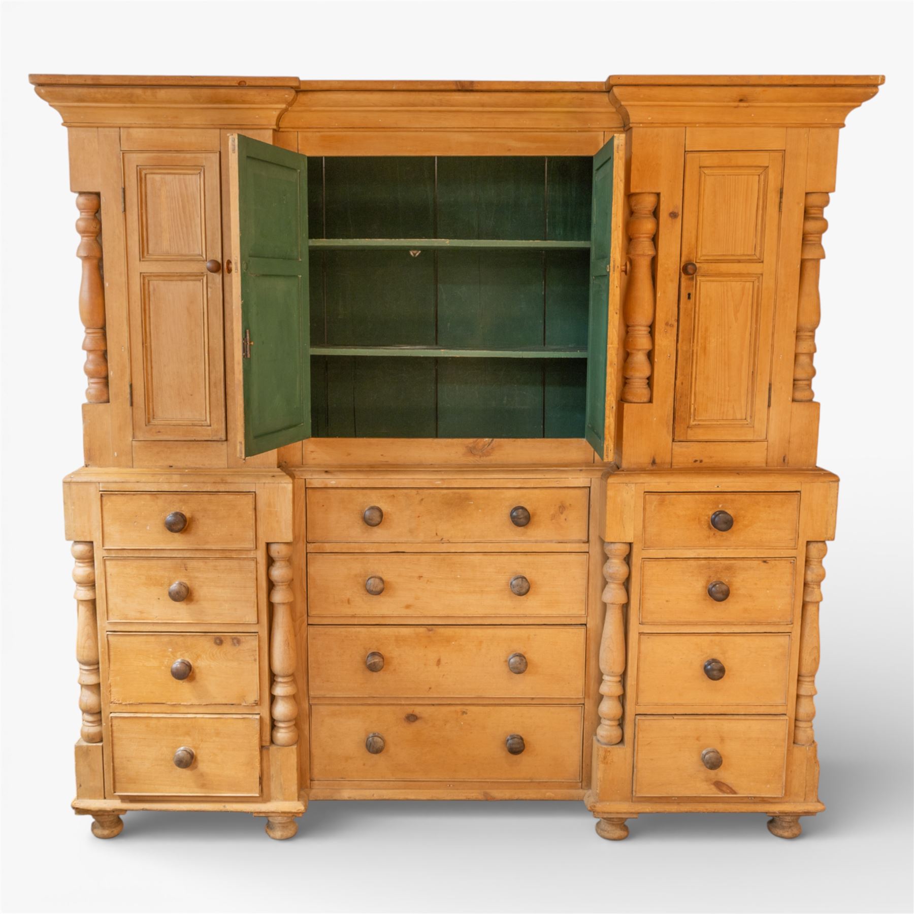 Large Victorian stripped pine reverse breakfront housekeeper’s cupboard, the moulded cornice above a central pair of panelled cupboard doors flanked by single cupboard doors and divided by turned baluster pilasters, the lower section fitted with an arrangement of twelve drawers with knob handles, raised upon bun feet