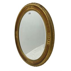 Oval wall mirror, in gilt frame decorated with scrolled foliate and scalloped outer edge, bevelled plate 