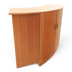 Turnidge of London - Mid 20th century teak drinks cabinet, shaped top with hinged fold-out side sections, twin doors with recessed handles enclosing fitted shelving and serving surfaces, sliding glass doors to the back, on a plinth base above castors