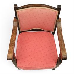 Early 20th century small oak open armchair, arched upholstered back with brass stud border over shaped seat cushion upholstered in pink foliate fabric, shaped open arms on square supports