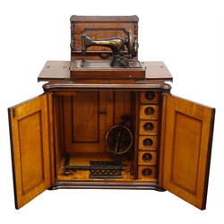  Singer treadle sewing machine with gilt transfer detail, in late 19th century walnut two tier cabinet with folding top above two burr panel doors, the maple interior with five drawers, W78cm, H98cm, D55cm   