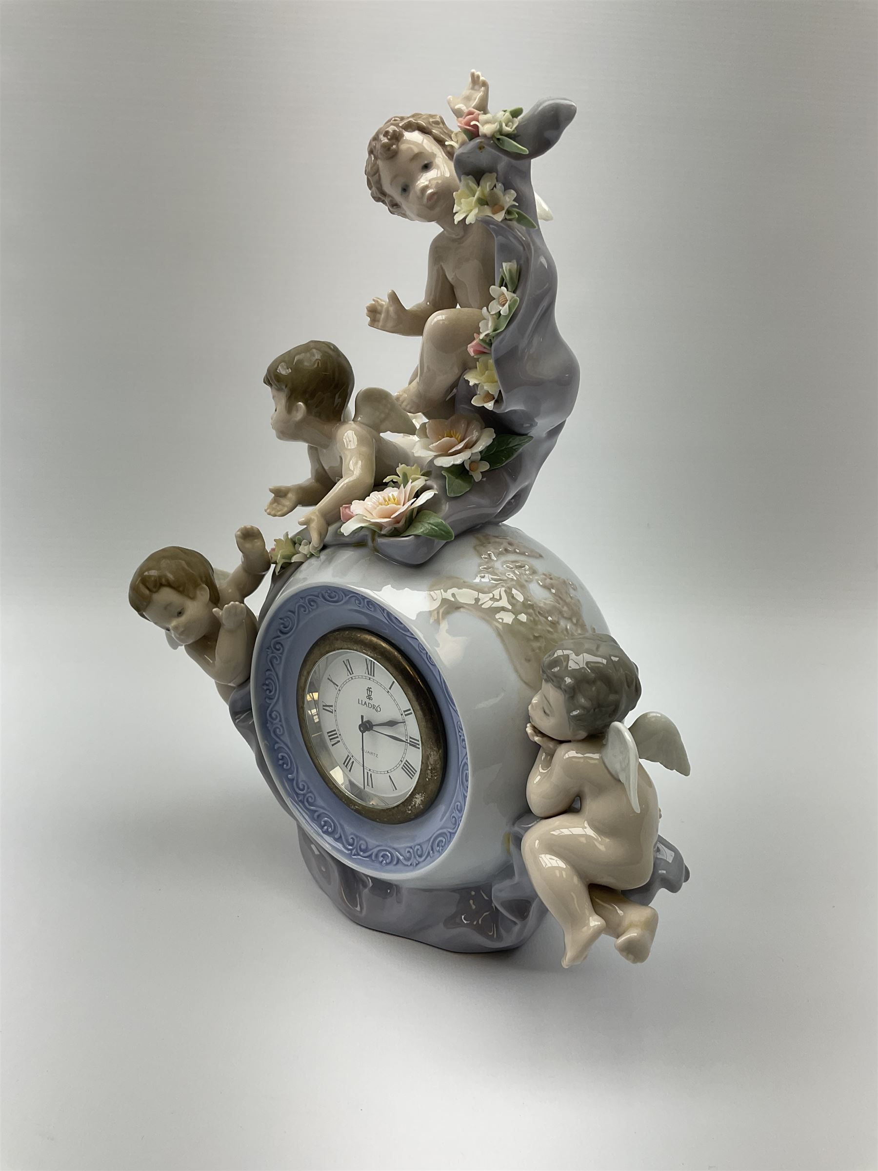 A Lladro mantel clock modelled as a globe with inset clock, surmounted by four putti and floral garlands, with blue printed mark and impressed 5973 beneath, H29cm.