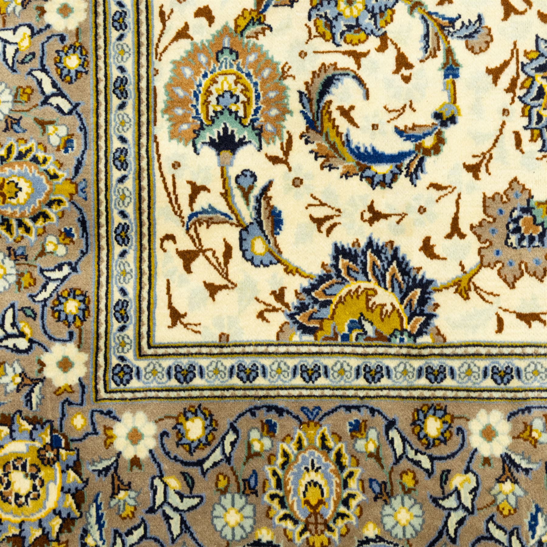 Central Persian Kashan hand-knotted carpet, ivory ground, with an all-over floral design of palmettes, scrolling vines and flowerheads in blue, ochre and beige tones, enclosed by a sage green border with repeating floral sprays and leafy scrolls, flanked by narrow guard stripes, with cotton fringes
