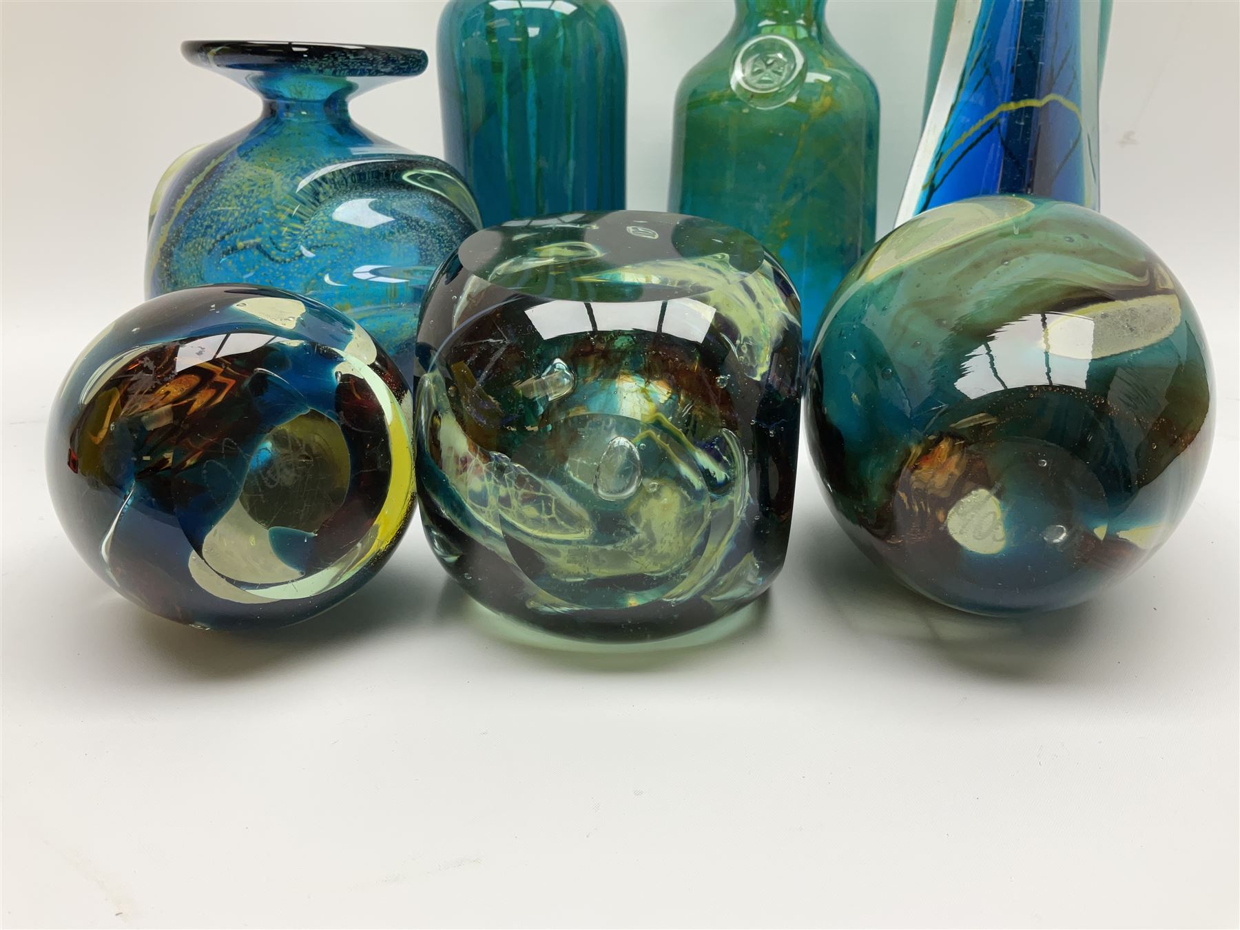 Quantity of M’dina art glass to include a streaked blue and green bottle form vase with captured bubble design and slender neck, H35cm, along with a paperweight, ovoid form vase and another vase all decorated in a blue, brown and white colour way, other contemporary glass examples etc with etched marks beneath