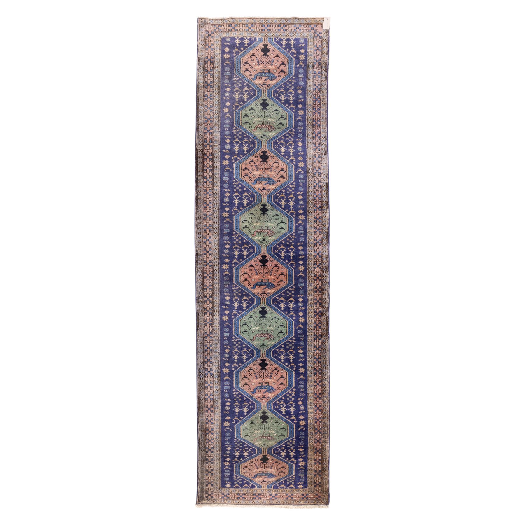 North West Persian Ardebil hand-knotted runner, indigo field composed of a vertical series of large linked hexagonal medallions alternating soft terracotta and sage-green grounds, medallions connected narrow waist panels, surround field filled with geometric devices on a pale blue ground, principal border decorated with a repeating geometric and floral motif on a light ground flanked by narrow guard stripes incorporating small rosettes, with cotton fringe ends 