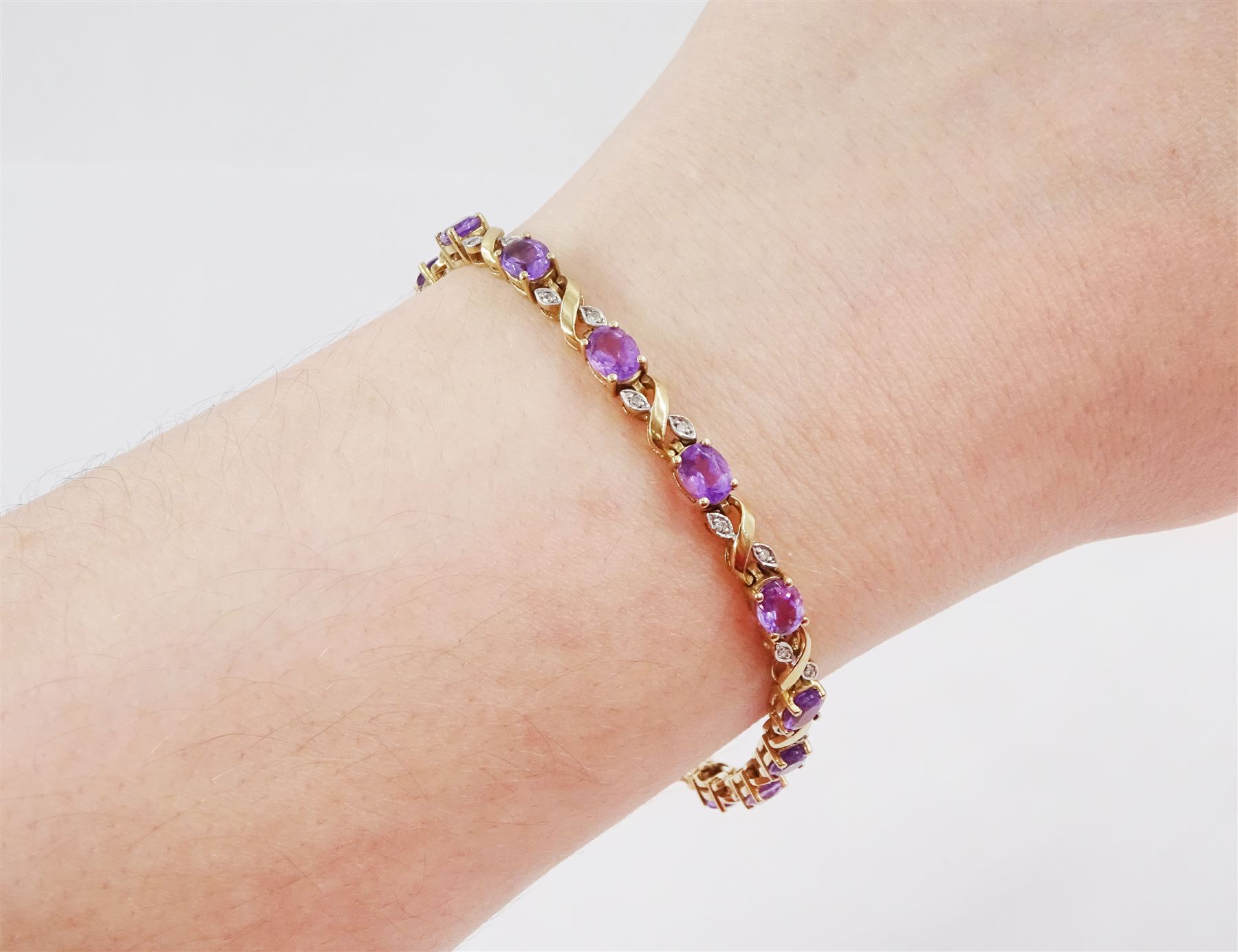 9ct gold amethyst and diamond bracelet, fifteen oval cut amethysts each spaced by two diamond chips in a crossover marquise setting, hallmarked