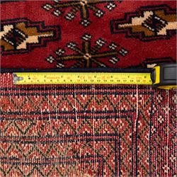North East Persian Turkoman hand-knotted carpet, madder red field decorated with rows of repeating Tekke guls, in offset horizontal bands and interspersed cruciform subsidiary motifs, enclosed within narrow geometric borders featuring stylized tribal devices, with fringe ends   