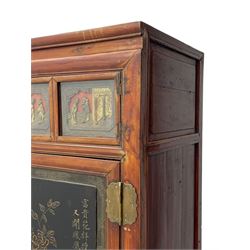 Late 19th century Chinese Qing dynasty red and black lacquered wood cabinet,  Fujianese province, upper cupboard enclosed by two doors with relief carved and gilt panels depicting figures behind glass, the large cupboard enclosed by two panelled doors carved with trailing foliate branches and birds, inscribed with Chinese characters, to the left ‘The red mountains are in the shape of Phoenixes and appear auspicious’ and to the right, ‘Wealth and honour are given by flowers and I hear the sound of the phoenix', fitted with two drawers, on square supports with carved brackets 