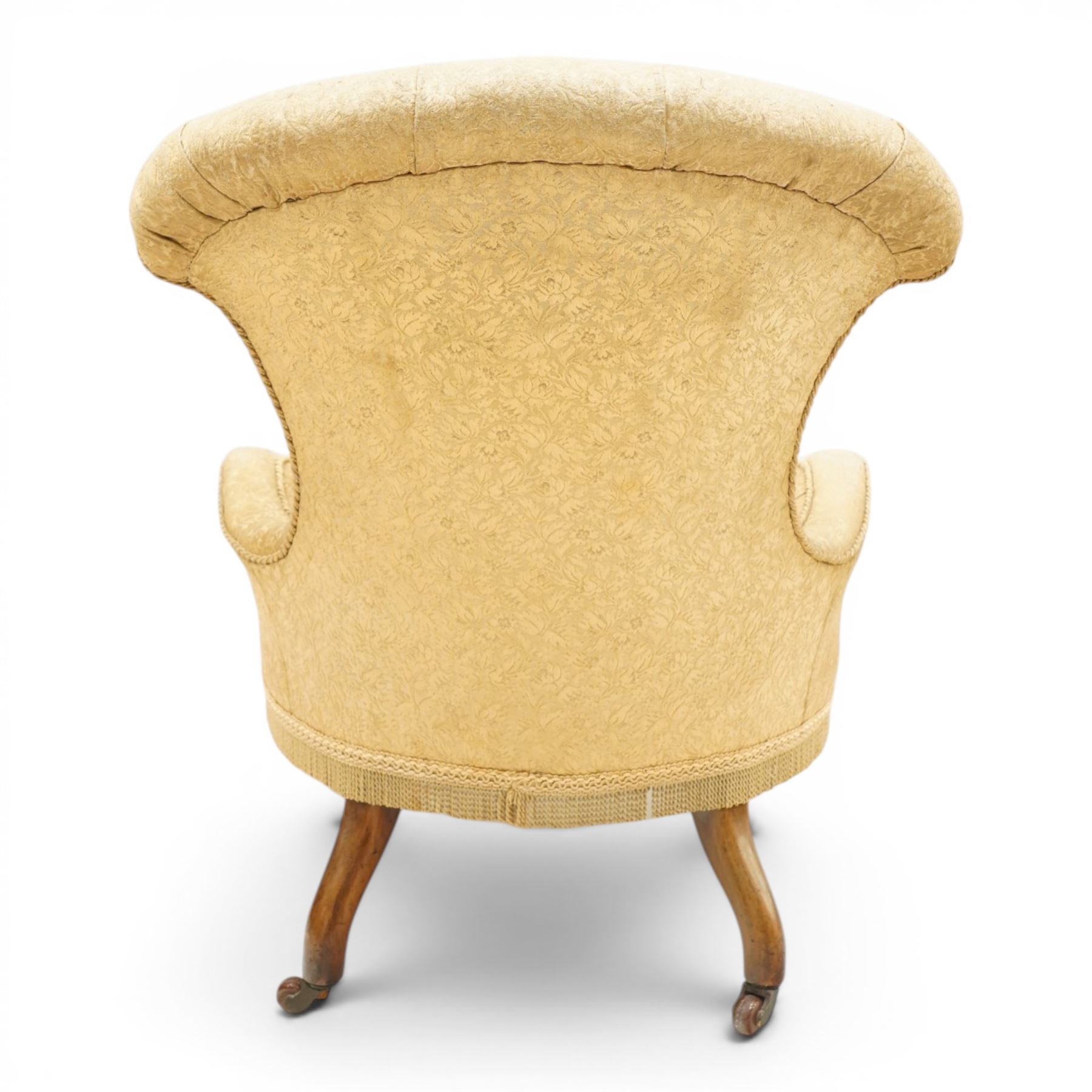 Victorian Aesthetic Movement walnut framed nursing chair, the fan back and sprung seat upholstered in buttoned foliate patterned gold damask fabric with fringing, raised on beaded tapering fluted supports with ceramic castors