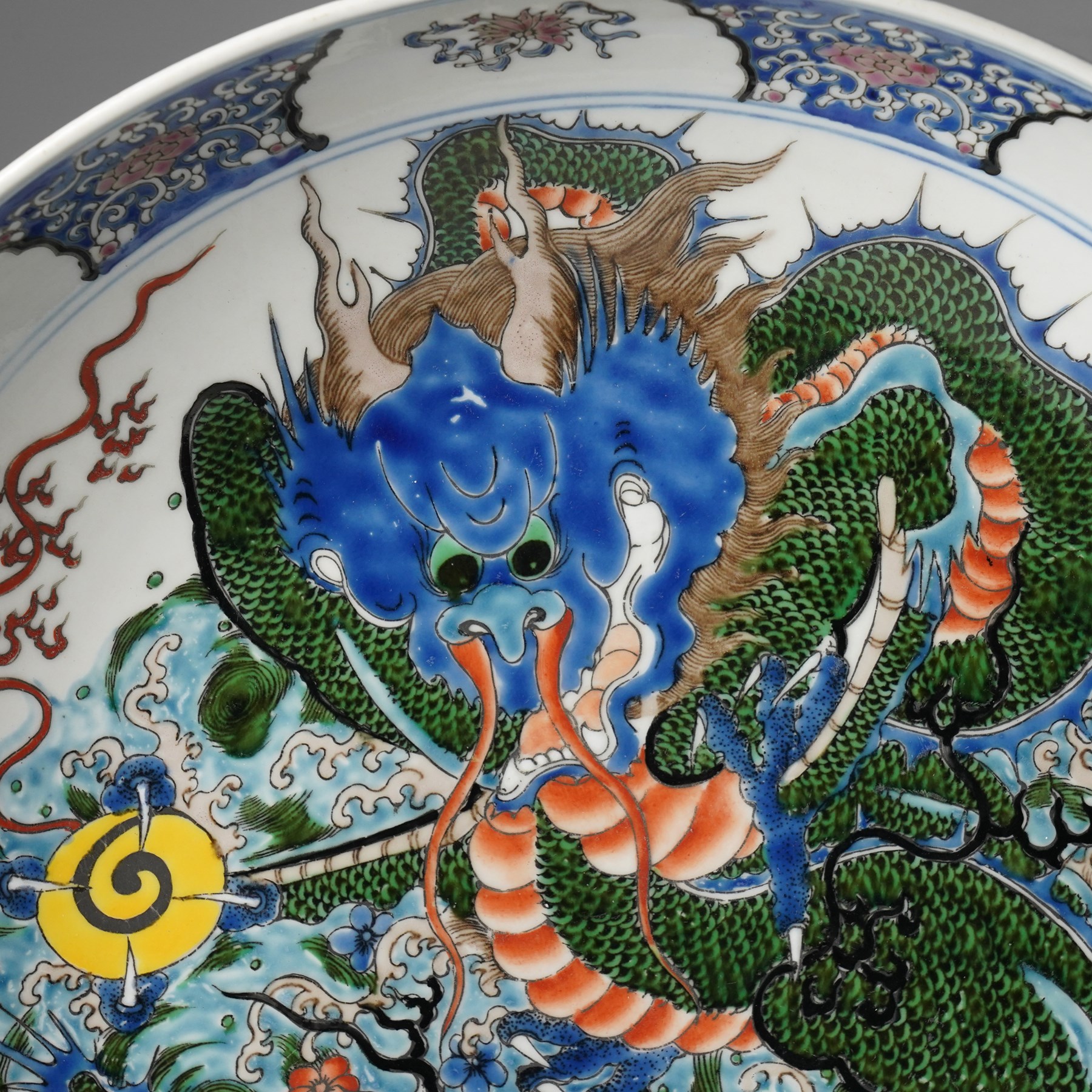 Chinese charger, decorated in blue, green and red enamels with a four clawed dragon chasing the flaming pearl amidst waves and flower heads, the rim with border of alternating reserves of auspicious emblems and flower scrolls, bearing apocryphal Kangxi mark beneath, D38cm 

