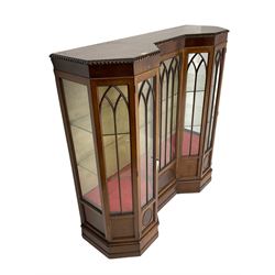 Early 20th century mahogany Gothic style display cabinet, faceted reverse break front, enclosed by three doors with pointed arch astragal glazing, on stepped and moulded plinth base