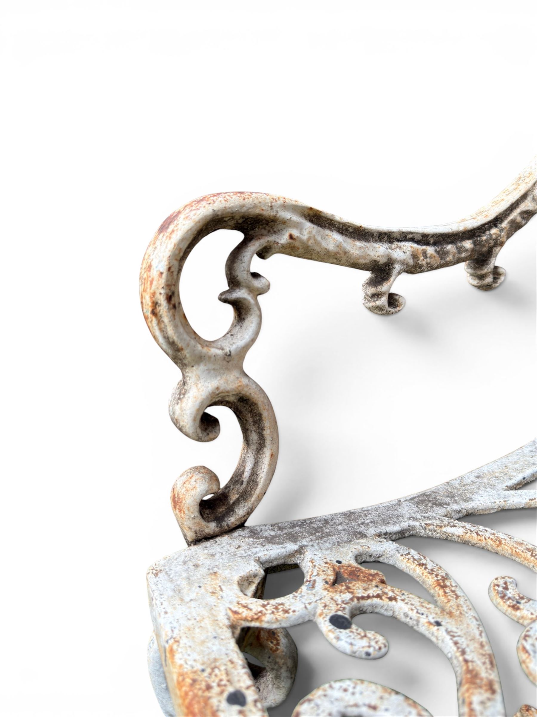 Pair of Victorian cast iron garden chairs, the ornate pierced back of scrolling foliate design, scrolling arm terminals over splayed supports formed of C and S-scrolls, in distressed white painted finish