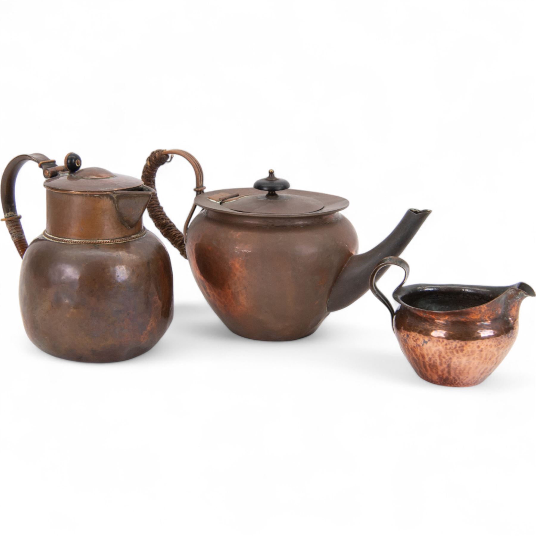 Keswick School of Industrial Arts: Arts & Crafts copper teapot, of stylised squat form with cane bound reed handle and ebony finial, together with a lidded jug, of bellied form with cane bound handle and Bakelite type thumbpiece and a cream jug of squat form with stylised loop handle, all stamped KSIA beneath, tallest H14cm