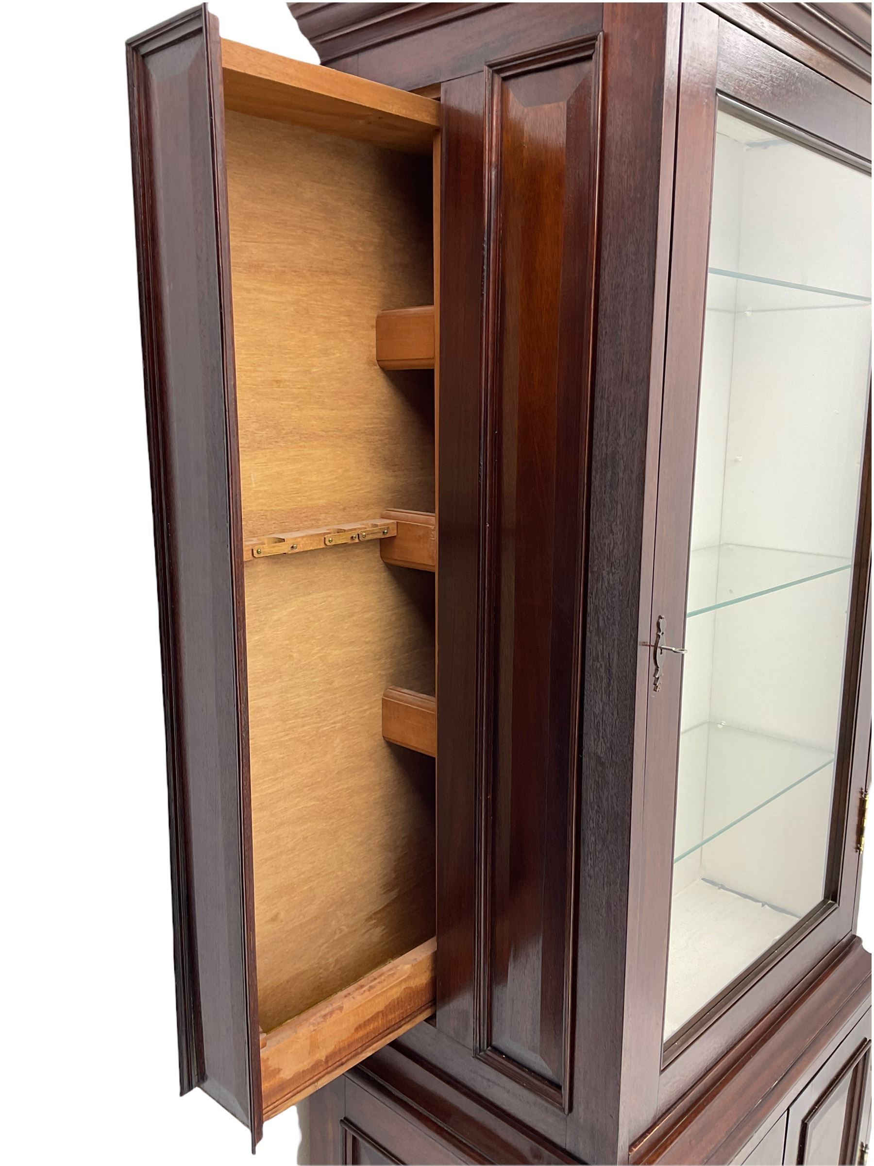 Mahogany display cabinet with hidden compartment, projecting cornice over single glazed door enclosing glass shelves, double panelled cupboard below, the interior with button releasing sliding back compartment, on bracket feet