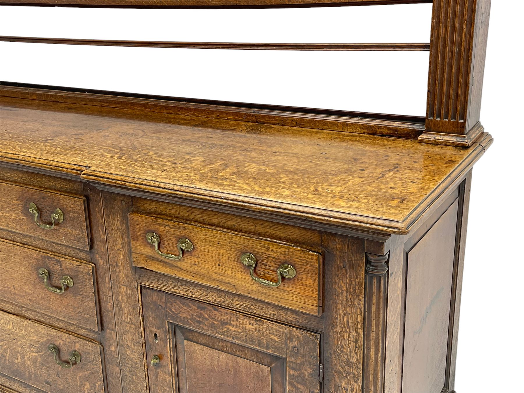 George III oak dresser, projecting dentil cornice over three heights plate rack enclosed by fluted uprights, the dresser fitted with five drawers and two panelled cupboards, canted corners with fluted quarter columns, on bracket feet