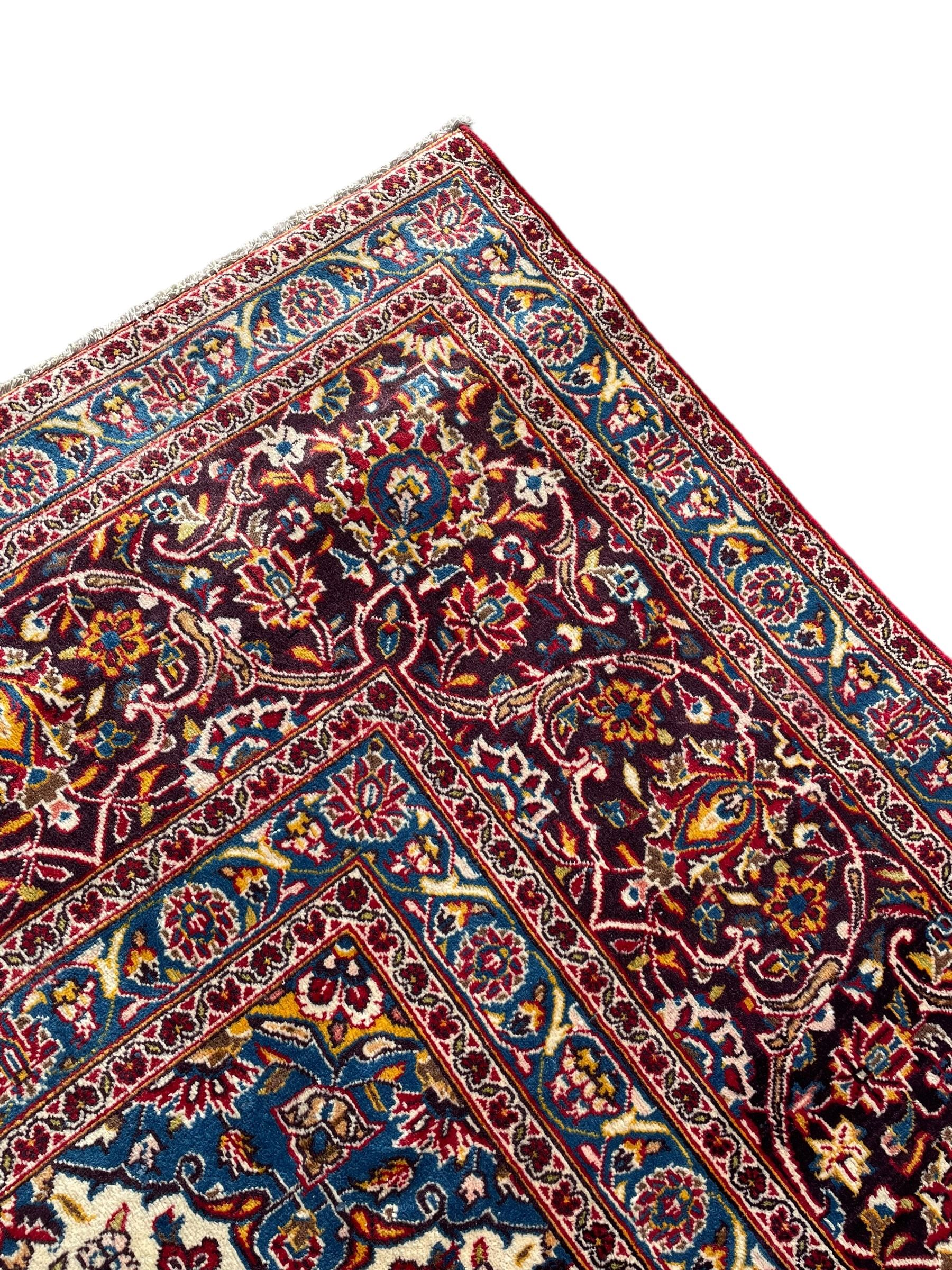 Large Persian Kashan crimson ground carpet, large floral central medallion surrounded by trailing branches decorated with leaves and stylised plant motifs, the main border with scrolling design interspersed with palmettes, within floral pattern guard stripes 