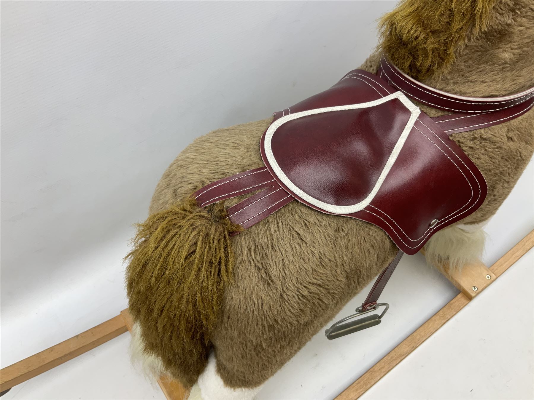 Modern plush covered rocking horse with inset eyes, simulated leather bridle and saddle with metal stirrups, on curving wooden rockers L94cm H64cm