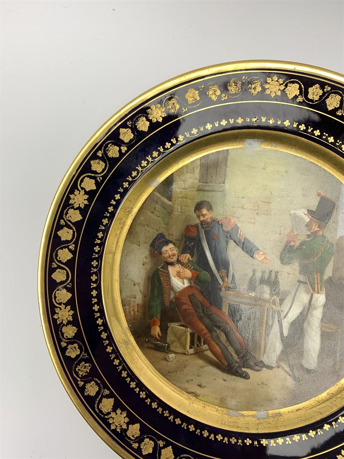 19th century Rihouet Paris porcelain cabinet plate, decorated with a central panel illustrating three French soldiers around a bottle laden table, one surveying a note, within a dark blue gilt detailed border, with French inscription verso, and red printed mark Rihouet Rue de la Paix A Paris and green fish mark, possibly for Perche, D23cm 



