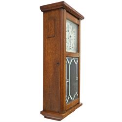 Art Deco style oak wall clock, moulded cornice above a silvered dial with Arabic numerals and geometric spandrels, glazed door with geometric bevelled glass panels enclosing a circular pendulum, on a stepped moulded base