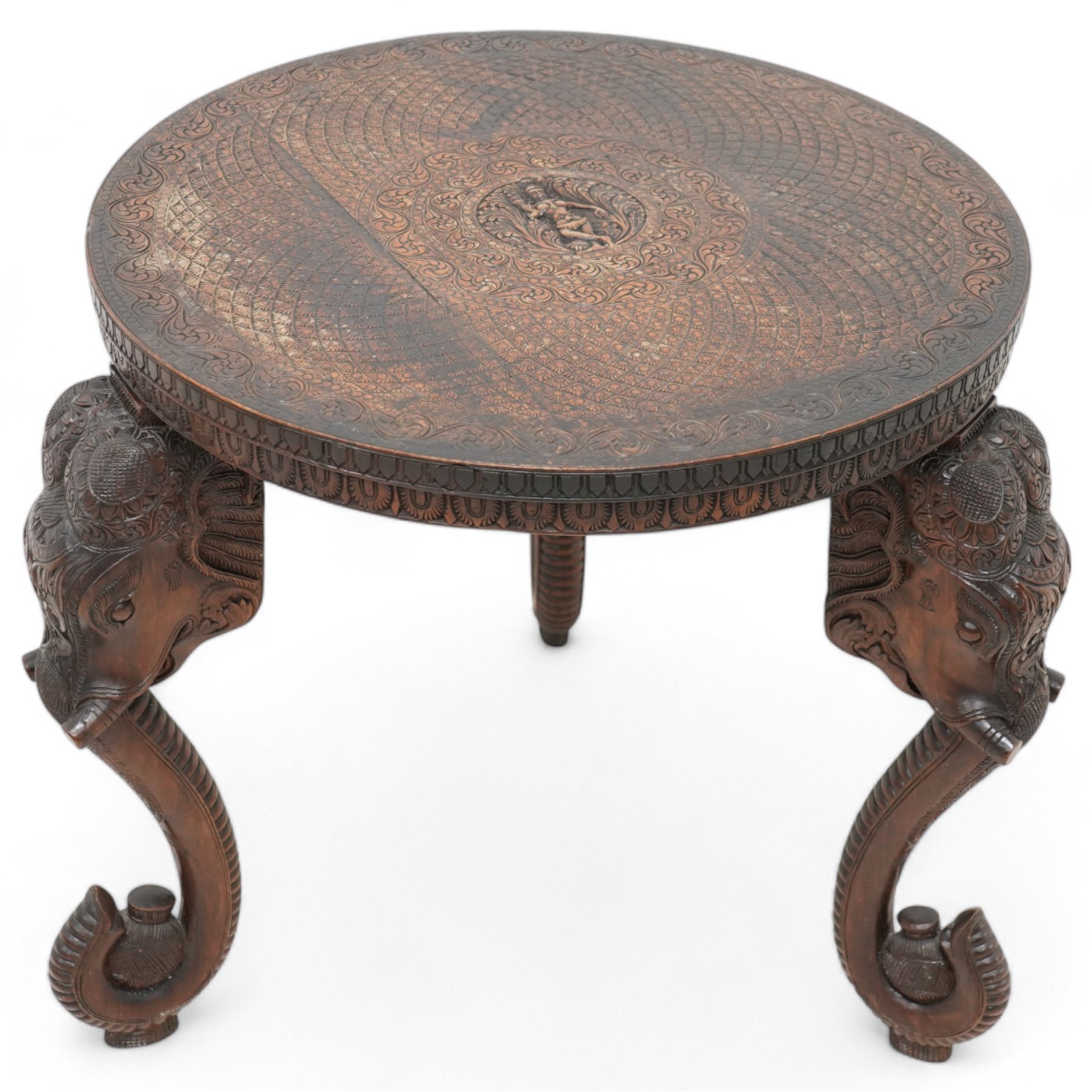 Anglo-Indian hardwood occasional table, circular top carved with concentric pattern and scrolling foliage, on three elephant carved supports decorated with flower heads