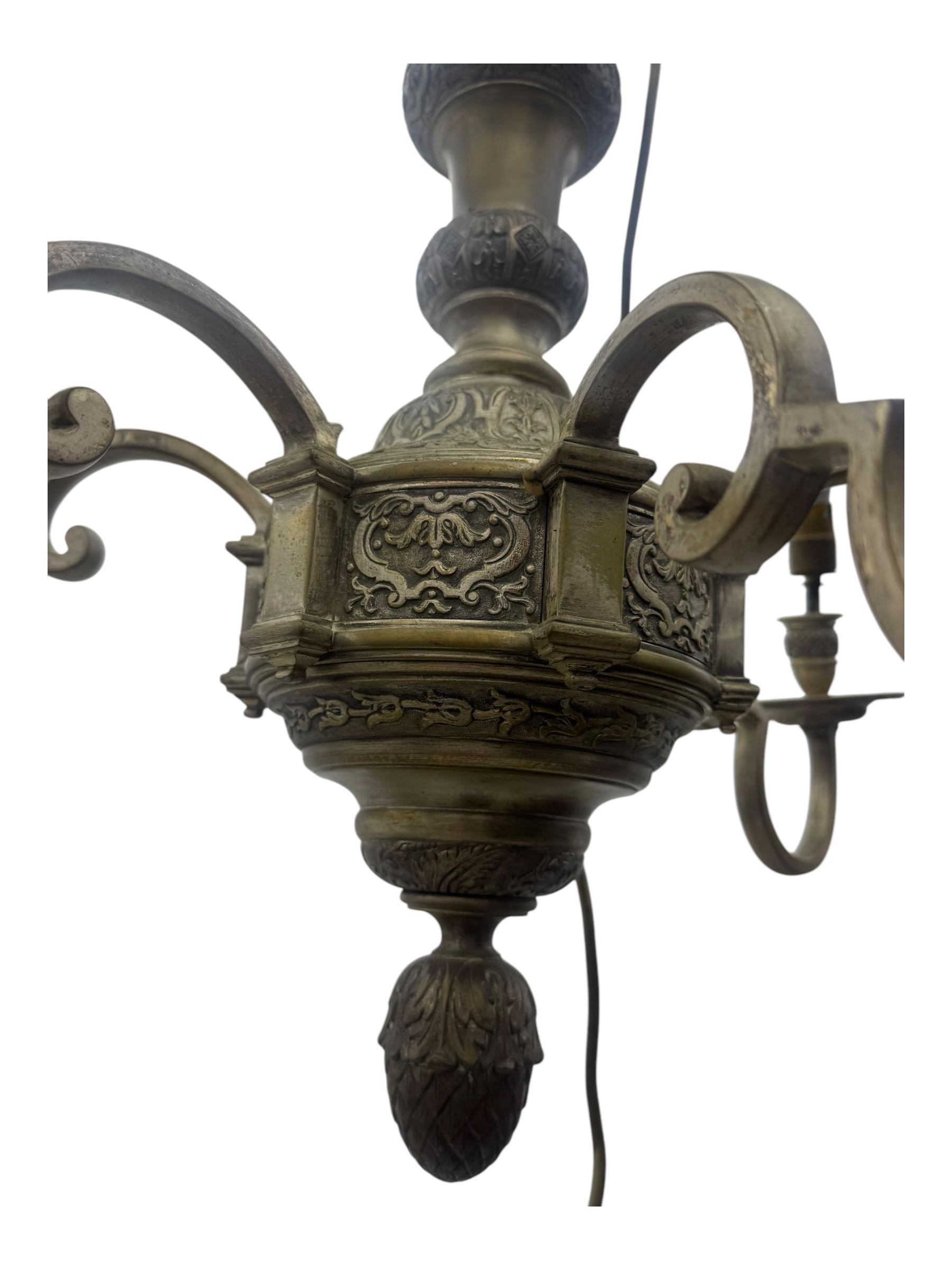 Pair of mid-20th century brass chandeliers, each with cast foliate and scroll decorated central body, issuing six scrolling arms with circular drip pans and bulb holders, suspended from integral ceiling loops