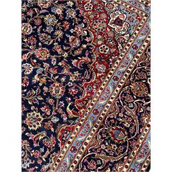 Persian Kashan indigo ground carpet, central floral pattern medallion surrounded by a densely decorated field depicting trailing branches with leaves and palmettes, scrolling border decorated with stylised plant motifs, within floral pattern guard stripes 